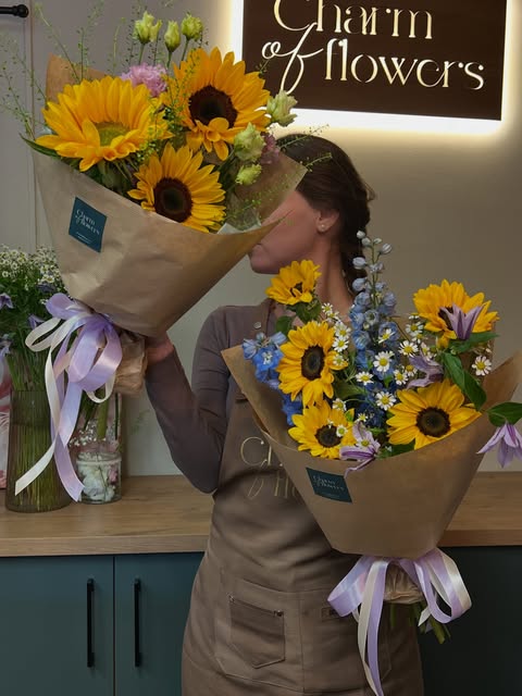 Floristka za pultem prodejny se dvěma kyticemi ze slunečnic